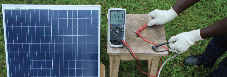 A solar panel and somebody's hands taking measurements. This photo was taken as part of the Envidatec and GIZ project 'Promotion of Renewable Energy and Energy Efficiency programme (PREEEP)' in Uganda.